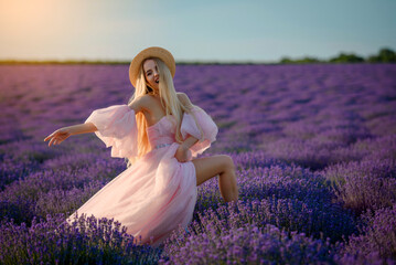 Portrait of a young beautiful happy smiling woman in a pink dress and a hat  walking in the lavender field