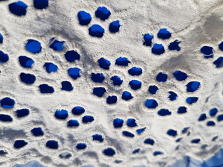 Wavy white embroidered fabric with small round holes with a floral print, on a blue background (macro, top view, diagonal, texture).
