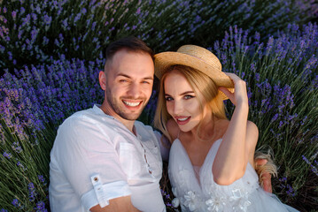 a woman in a white dress and hat and a man in a white shirt are walking in a lavender field..