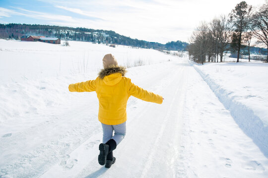 Outdoors in winter, a little girl in a yellow jacket walks along a snowy road.