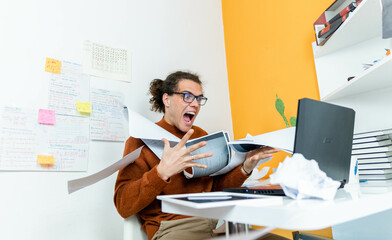 a young nervous businessman screaming in the office and throwing away papers, working from home...