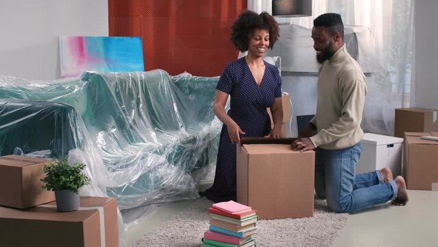 Happy African-American couple pack stuff on moving day in old house