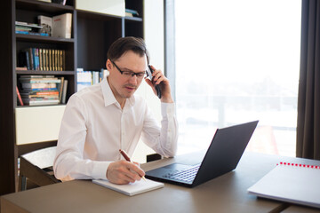 man businessman working in office or at home at table on laptop, talking on phone
