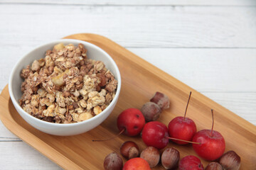 a bowl of granola, apples and filbert on wooden tray