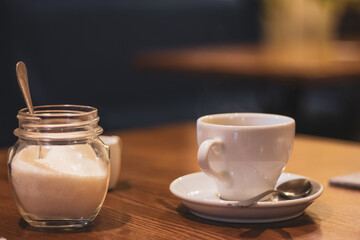 Coffee cup, sugar and milk. Morning drinks concept. Breakfast still life. Espresso in white cup with spoon and sugar. Hot drinks. Morning latte. Aroma beverages. Cafe interior. 