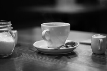Coffee cup, sugar and milk, black and white. Morning drinks concept. Breakfast still life, monochrome. Espresso in white cup with spoon and sugar. Hot drinks. Morning latte. Aroma beverages