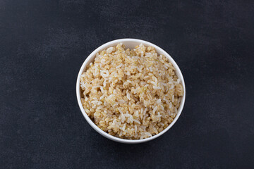 Brown rice in white rice bowl isolated on black background.