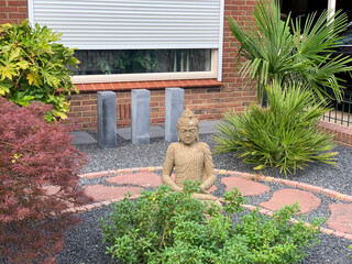 Beautiful oriental style house entrance with cement Buddha statue and stone garden path and oriental plants: acer japonicum, fatsia japonica and palm