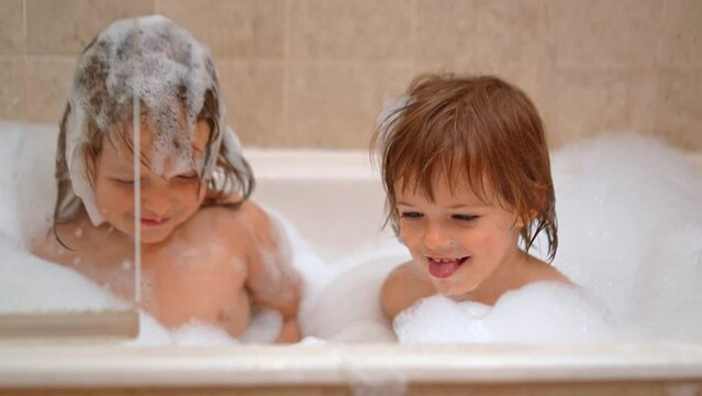 Adorable sisters - baby girls playing with Soap Foam in the bath. Fun and children hygiene concept