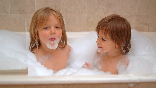 Adorable sisters - baby girls playing with Soap Foam in the bath. Fun and children hygiene concept