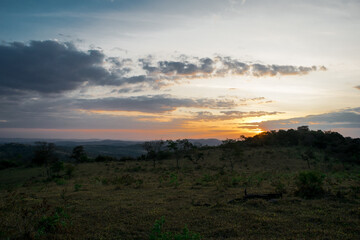 Lindo pôr do sol com nuvens e silhueta de árvores ao entardecer, com céu azul e limpo, de cima de montanha no bairro Jardim das Oliveiras, Esmeraldas, Minas Gerais, Brasil