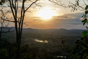 Lindo pôr do sol com nuvens e silhueta de árvores ao entardecer, com céu dourado e limpo, de cima de montanha com lago  ao fundo, Esmeraldas, Minas Gerais, Brasil