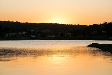 Lindo pôr do sol ao entardecer com céu dourado e limpo, com reflexo em lago no bairro Jardim das Oliveiras, Esmeraldas, Minas Gerais.
