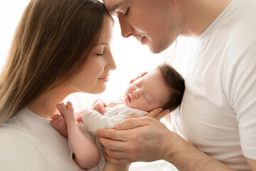 Obraz na płótnie Canvas Close up portrait of young parents and newborn baby. Father and mother kiss and hug a beautiful newborn daughter. The concept of love, happy fatherhood and motherhood. Photography on white background.