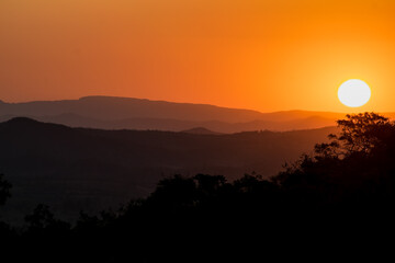 Pôr do sol com nuvens e silhueta de árvores ao entardecer, com céu dourado e limpo, de cima de montanha no bairro Jardim das Oliveiras, Esmeraldas, Minas Gerais, Brasil