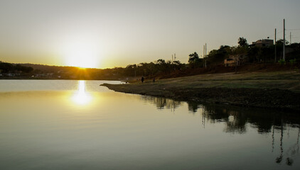 Pôr do sol ao entardecer com céu azul e limpo, com reflexo em lago no bairro Jardim das Oliveiras, Esmeraldas, Minas Gerais.