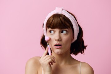 horizontal beauty photo of a funny, surprised woman with short hair holding a roller for massage, leaning it against her cheek and looking at the camera with her mouth wide open