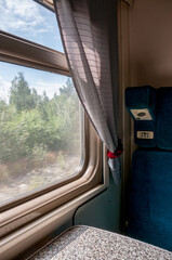 A window and part of the interior of a compartment car inside a traveling train in summer