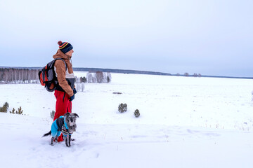 Fototapeta na wymiar young man in red brown warm clothes with backpack with mixed breed dog in warm blue suit walking in snow mountain looking at view of valley in winter Active lifestyle hiking pets adoption