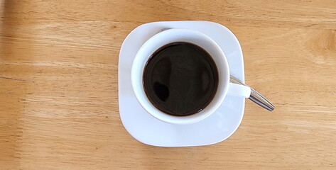 Top view of this white ceramic coffee mug resting on a rectangular coaster with stainless steel spoon. Fragrant hot espresso in a white mug placed on a wooden table.Caffeine refreshes the body.
