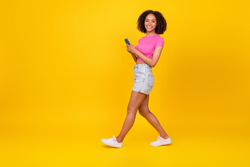 Fototapeta na wymiar Full size photo of nice brunette millennial lady hold telephone go wear top shorts shoes isolated on bright orange color background