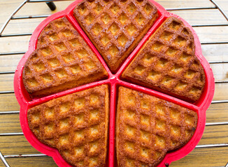 Freshly oven baked waffles in red plate on still rack in wooden background.