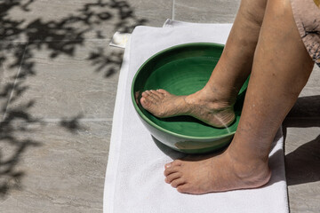 Elderly woman soaking feet with warm salt water at home.