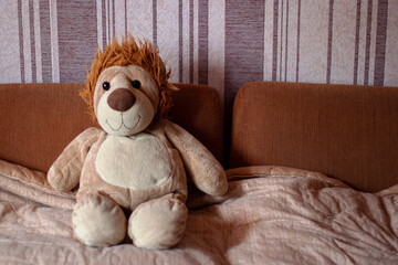 Plush toy lion, soft toy sits on a brown sofa. A cute brown lion is smiling at the camera. Toy portrait of a lion.