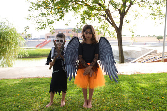 A girl dressed as a witch with an orange skirt and black wings and a boy dressed as a zombie scare the camera at a Halloween party. Trick or treat. 31st October. Happy halloween.