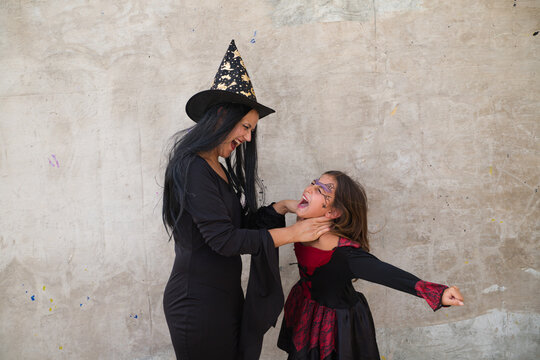 Happy halloween. Pretty young woman and girl dressed as witches on grey background play with terrifying and strangling gestures while having fun. Trick or treat.