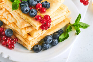 Pancakes. Stack of crepes or thin pancakes with berries, blueberries, red currants, raspberries and honey for breakfast. Homemade breakfast. Copy space. Selective focus.