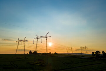 Dark silhouette of high voltage towers with electric power lines at sunrise