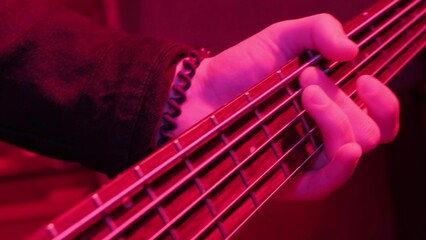 Hands of rock musician playing the electric bass guitar on repetition in red light