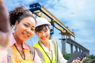 Positive confident diverse female engineers and architect in vest  and hardhats and with Tablet...