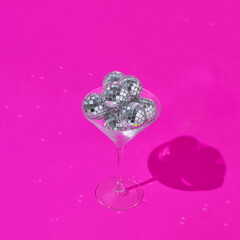 Martini cocktail glass with shiny disco balls on vibrant pink background. Minimal party concept. Retro 80s or 90s aesthetic.