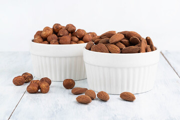 In white plates, almonds and hazelnuts on a light background.
