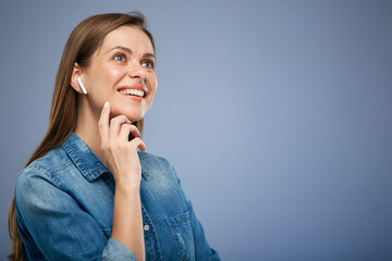 Smiling woman with one earphone, headphone or earbud in her ear touching her face with hand and looking up. Isolated portrait on blue background.