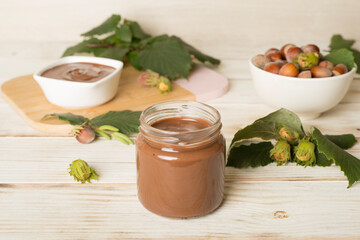 Hazelnut cream with nuts and green leaves on wooden table