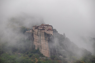 Fototapeta na wymiar Panoramic view of Holy Orthodox Monastery of Rousanou (St. Barbara), Kalambaka, Meteora, Thessaly, Greece, Europe. Unique rock formation are surrounded by mystical fog. Moody dramatic atmosphere