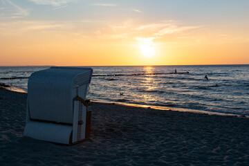 Sunset over the sea with beach chairs on the beach, one person is sitting on the wooden groynes