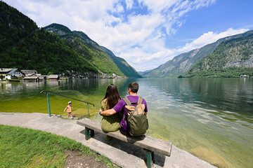 Couple with baby girl sitting on bench over Austrian alps lake in Hallstatt, Salzkammergut, Austria.