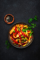 Asian cuisine, stir fry with chicken, red paprika pepper and zucchini bowl. Black kitchen table background, top view, copy space