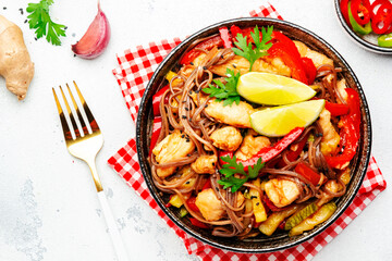 Asian cuisine, stir fry noodles with chicken and vegetables, paprika, zucchini and sesame seeds in bowl. White kitchen table background, top view, space for text