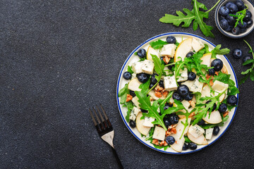 Delicious arugula salad with pears, blueberries, roquefort cheese and walnuts. Black kitchen table background, top view
