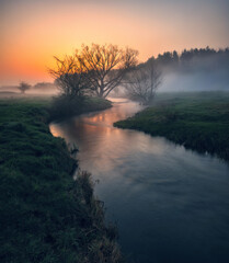 Beautiful spring sunrise over river banks. the sun's rays break through the mist. Morning fog