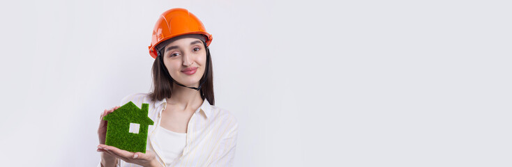 A young girl architect in a construction helmet demonstrates a model of a green house. Sale of ecological real estate.