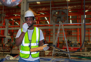 An African American male technician operates a machine inside a factory using a hydraulic crane switch.