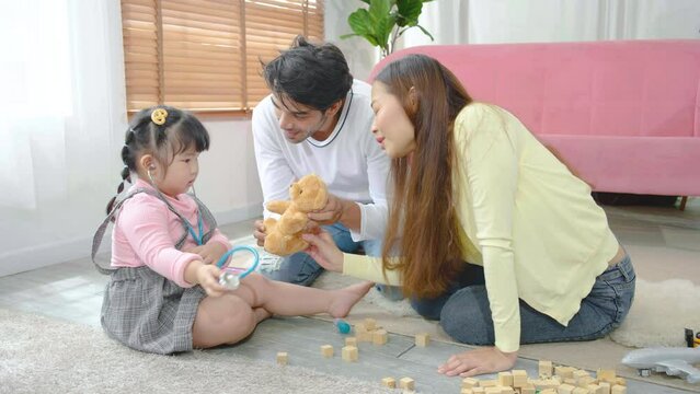 Little girl plays with teddy bear toy listens to him with a stethoscope with stepfather and mother, listening to teddy bear patient heartbeat and give injection, enjoying game
