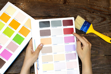 hands woman holding a color palette, guide of paint samples catalog with yellow blue brush on wood...