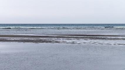 Obraz premium Wet sand. Gloomy seaside landscape. The harsh nature of the north of Europe. The cold coast of the Atlantic Ocean. Gray sand beach